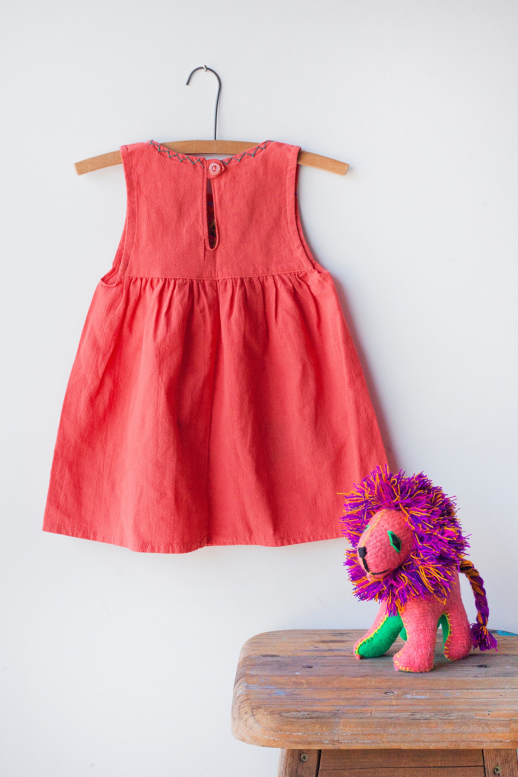 Reverse of kids sleeveless coral sun dress, showing coral button closure at neck.
