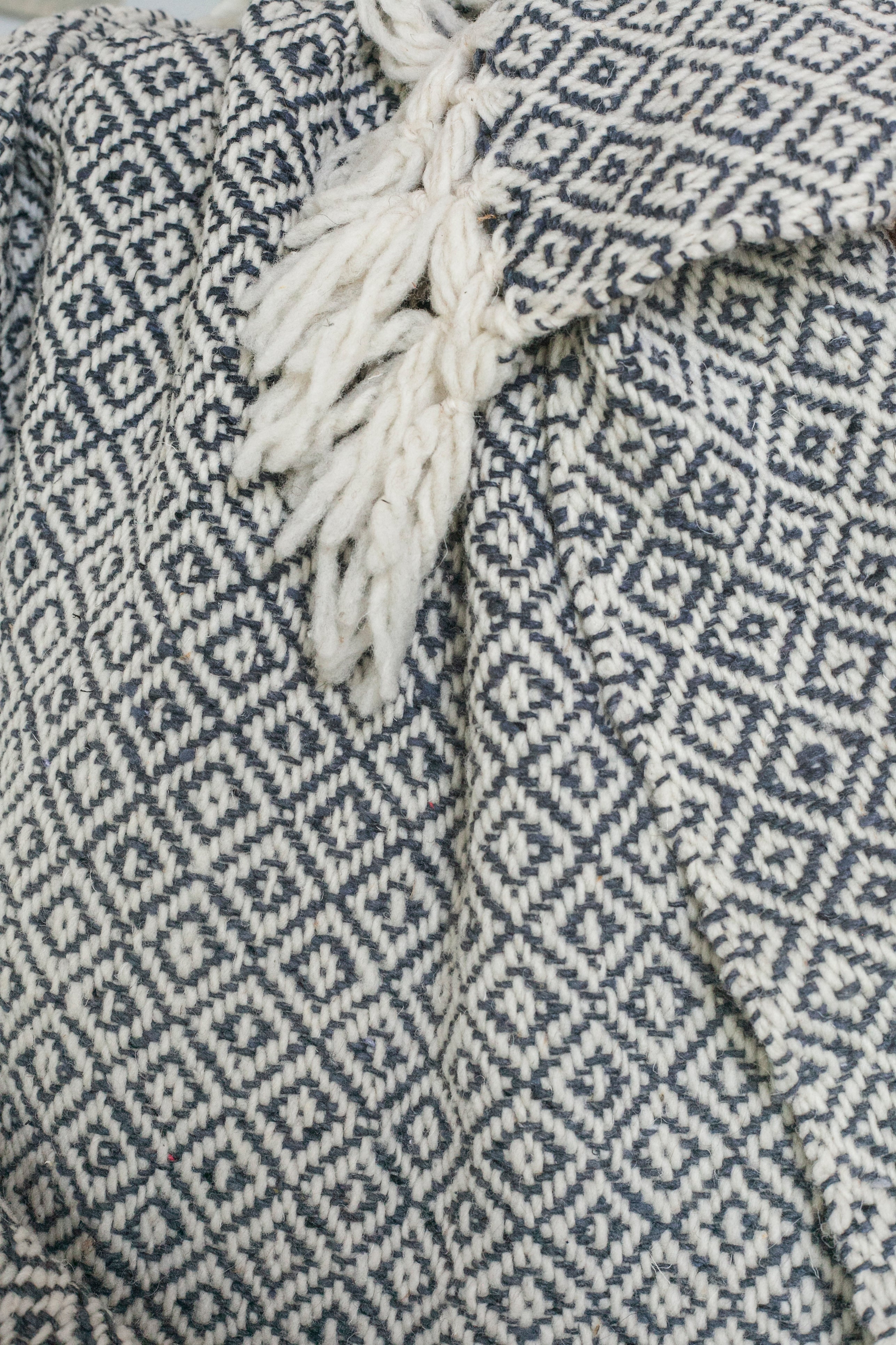 Detail of charcoal grey and white diamond weaving and tied tassels from a wool throw blanket