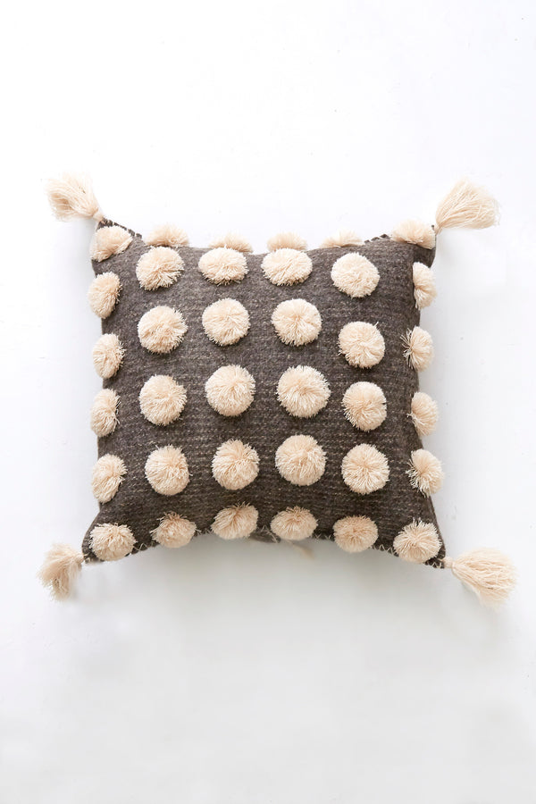 Square woven grey wool throw pillow covered in cream pom poms with cream tassels in each corner