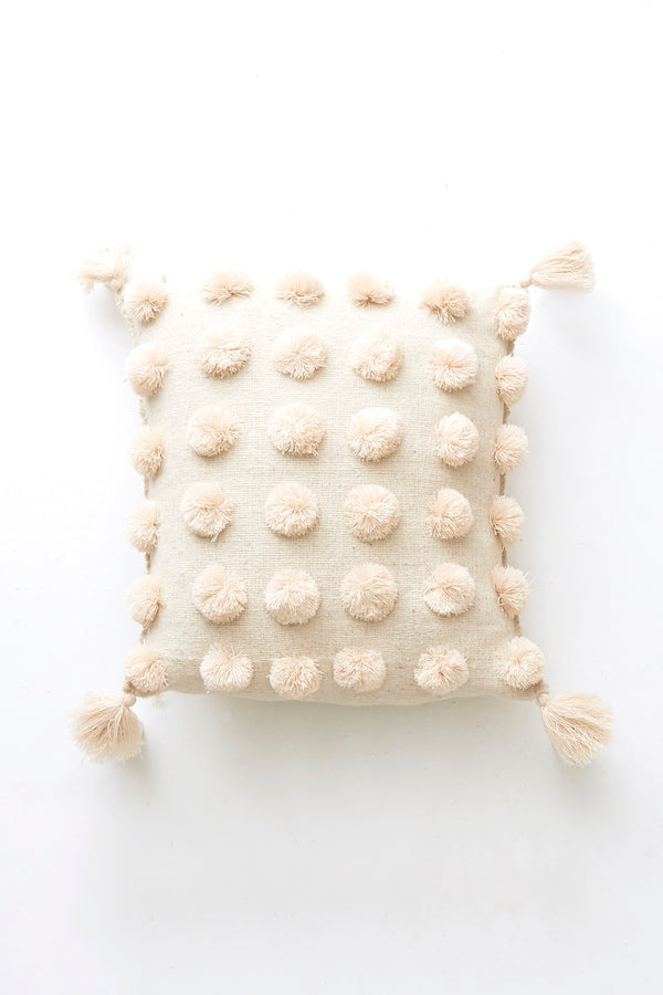Square woven wool cream throw pillow covered in cream pom poms with cream tassels in each corner