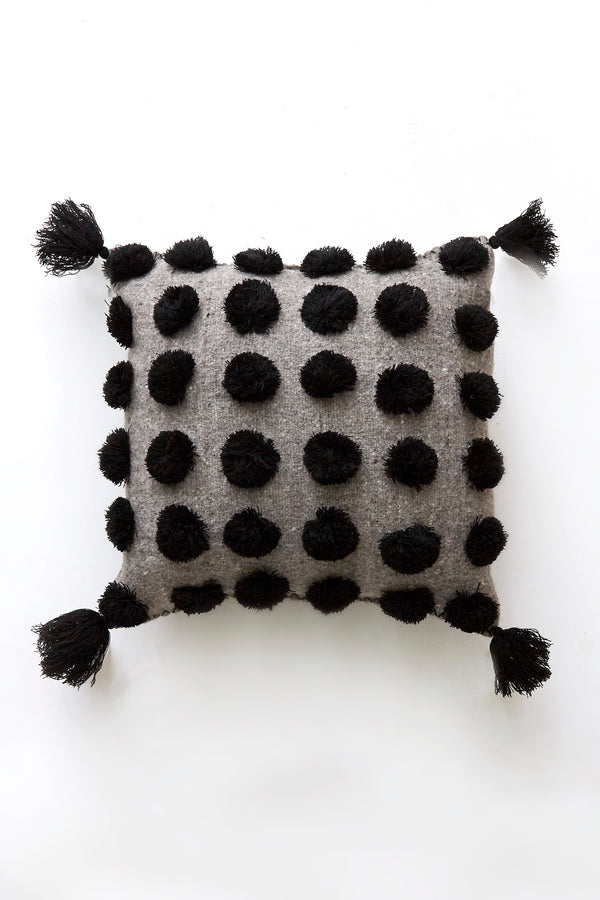 Square woven wool grey throw pillow covered in black pom poms with black tassels in each corner