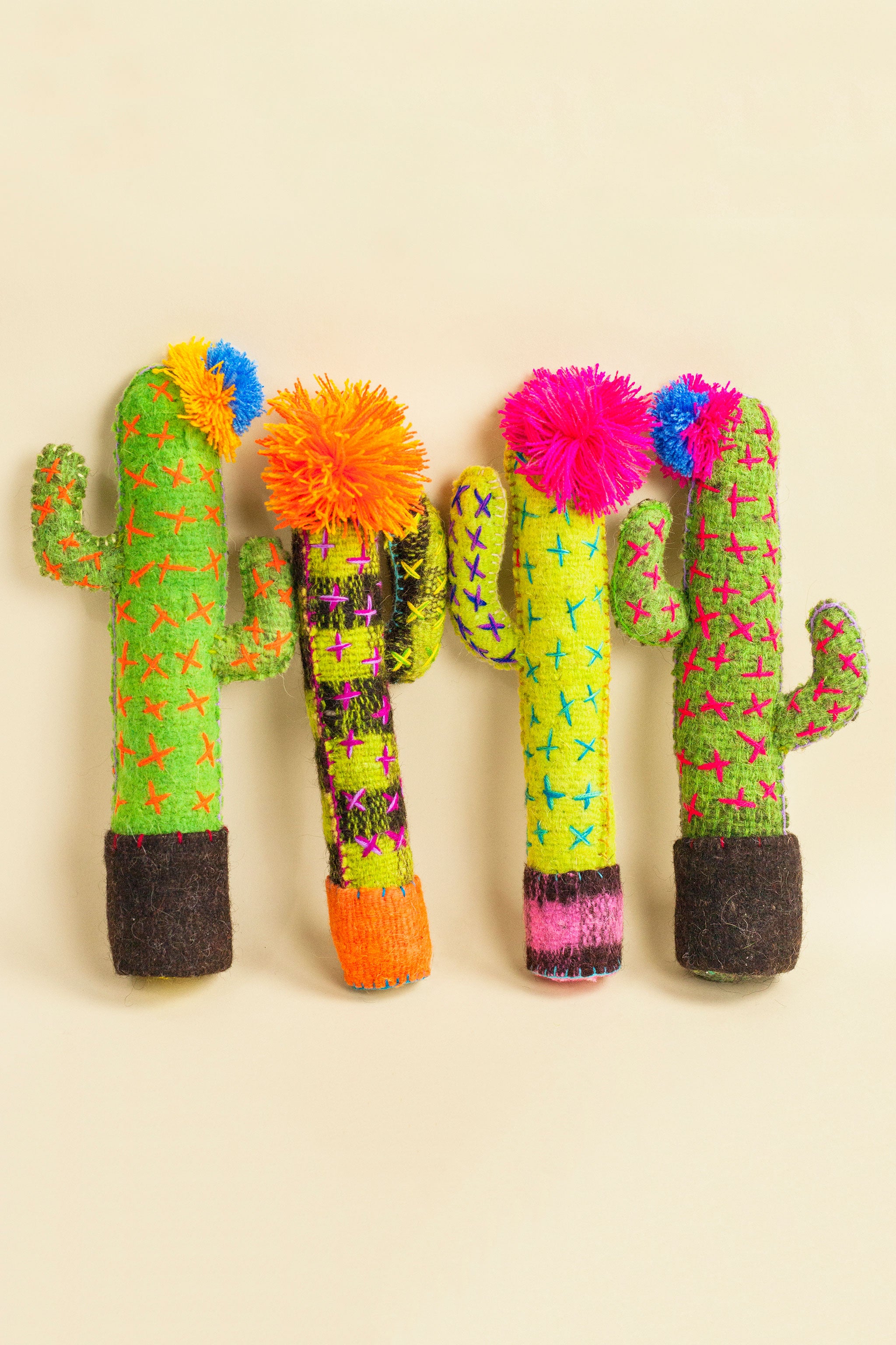 Standing felt cactus plush toys in different shades of green with hand-embroidered thorns and a colorful pom pom flower on top.