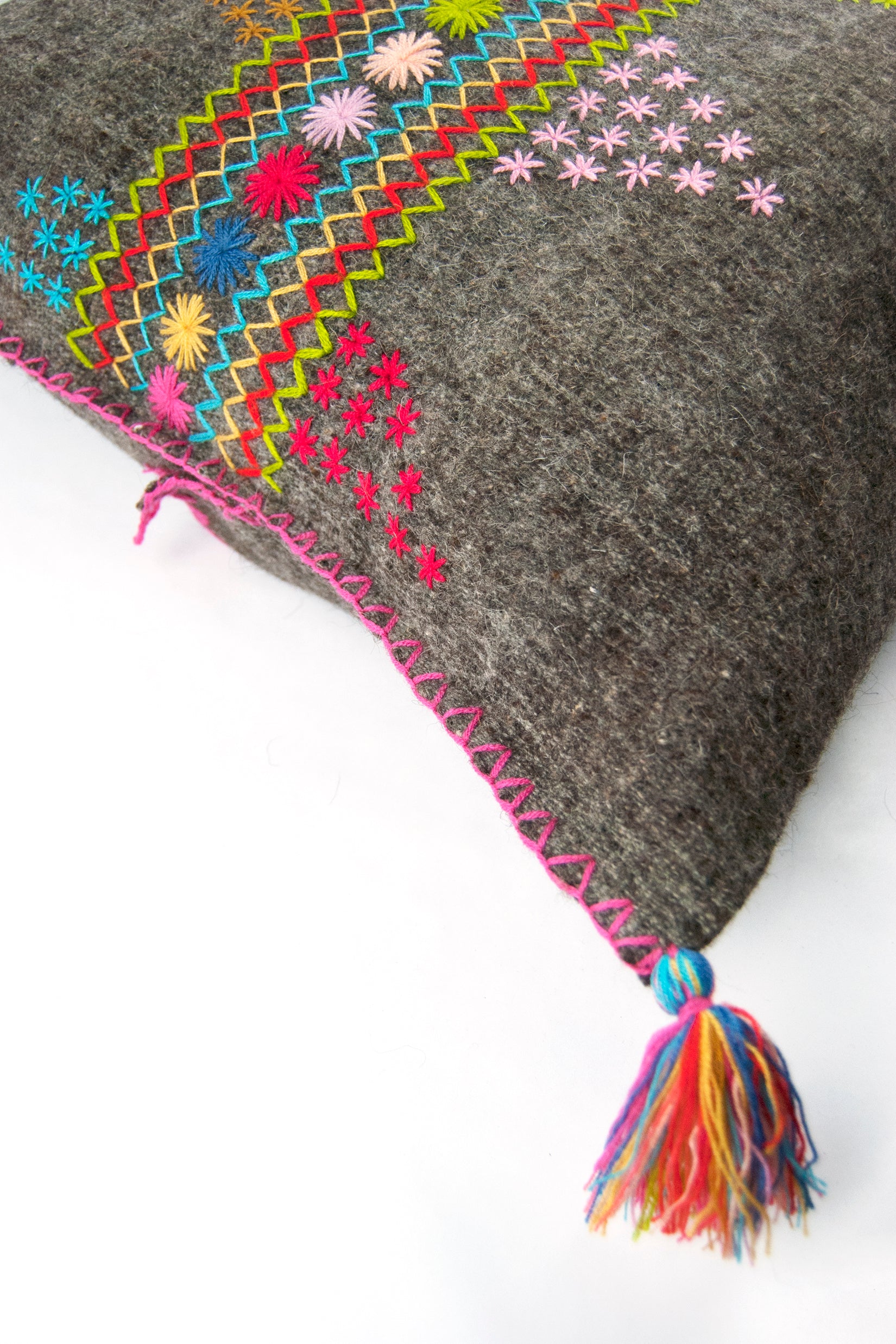 Detail of grey square woven wool throw pillow showing colorful embroidery and multicolor tassel