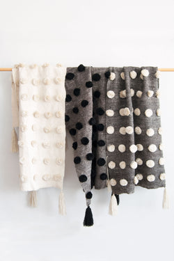 Three neutral wool throws covered in rows of neutral pom poms hanging together