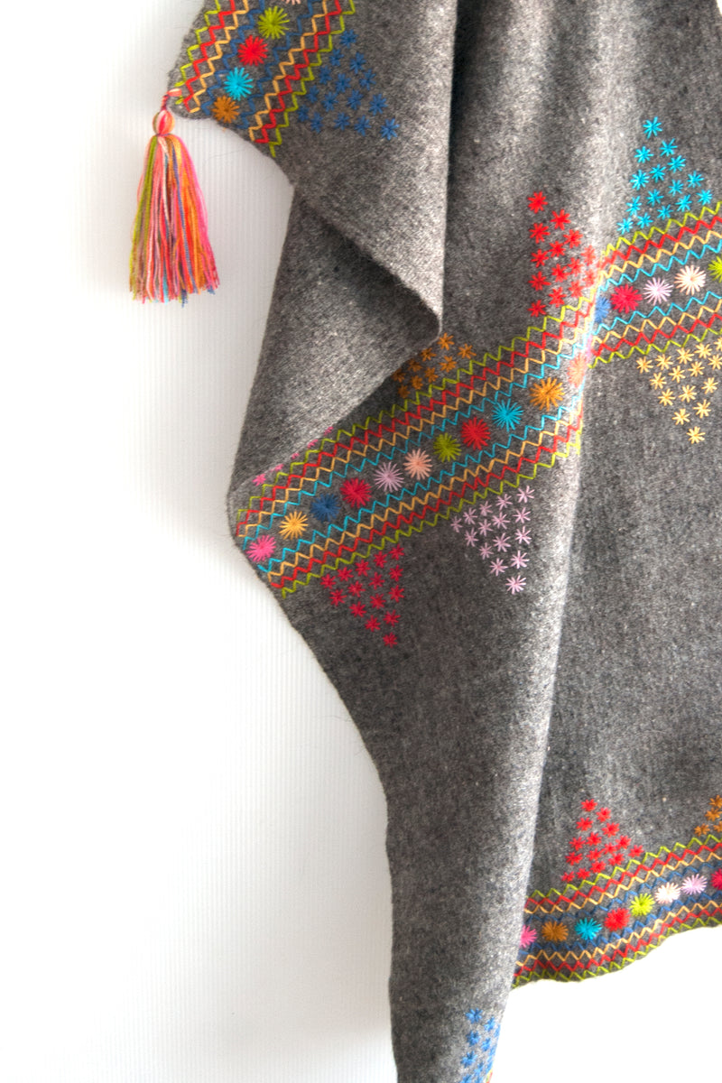 Detail of grey wool throw with colorful embroidered trim & accents and multicolor tassel at corner