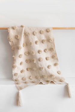 Cream wool throw covered in rows of cream pom poms with cream tassels at each corner