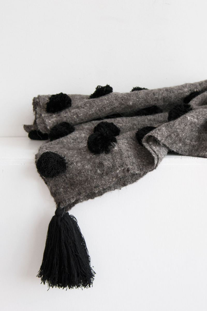 Detail of grey wool throw covered in rows of black pom poms with black tassel