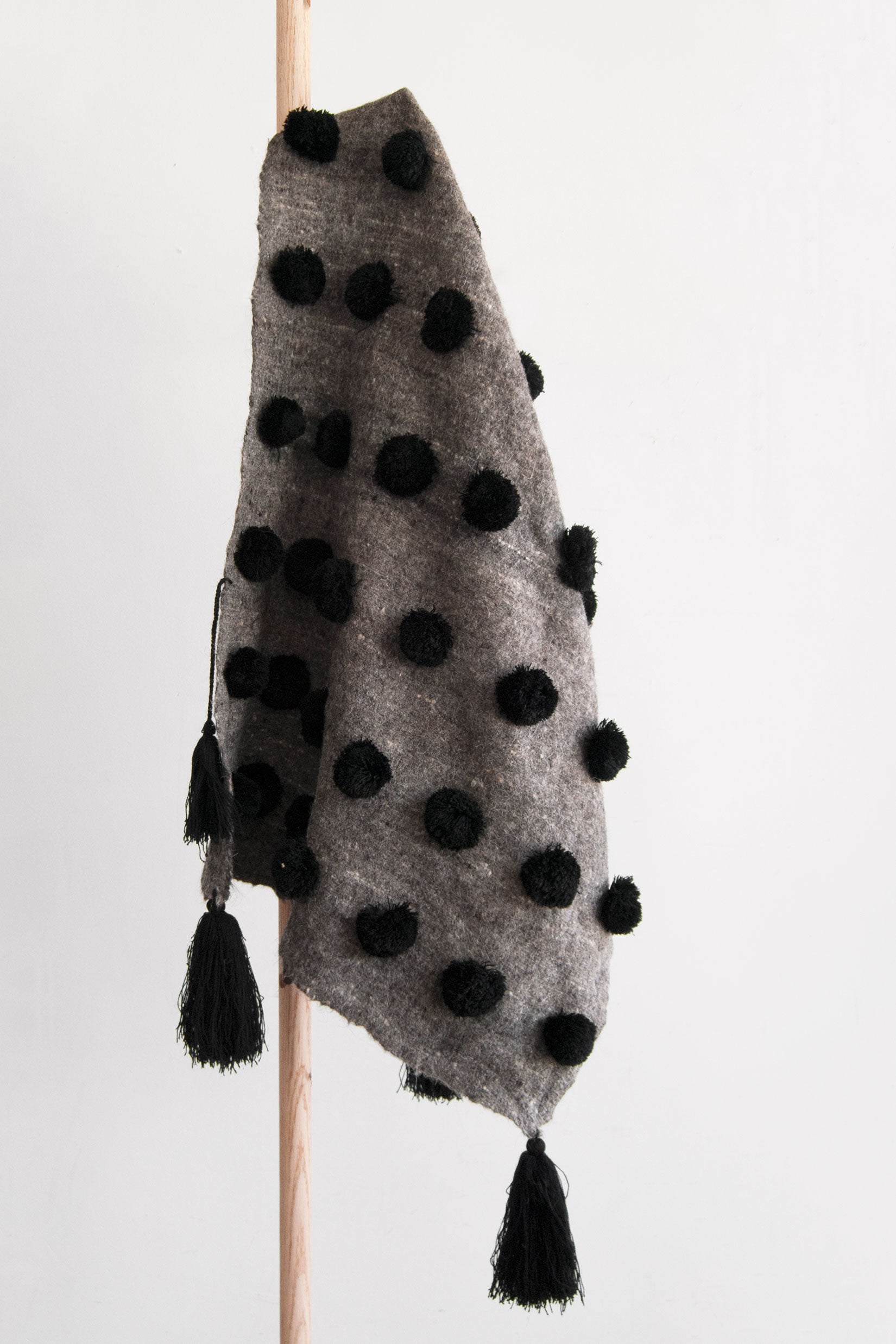Grey wool throw covered in rows of black pom poms with black tassels at each corner