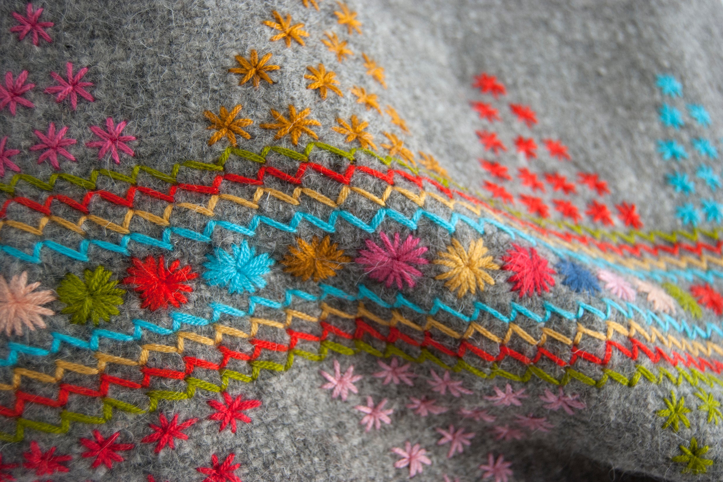Detail of grey wool throw with colorful embroidered accents