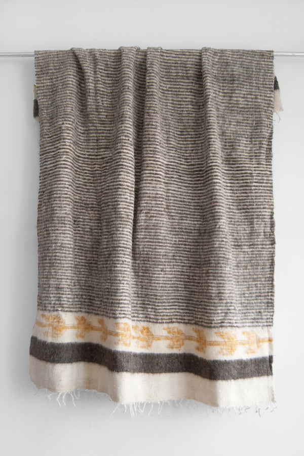 Queen sized ecru wool blanket with thin horizontal grey stripes throughout the body and gold arrow motif at both ends