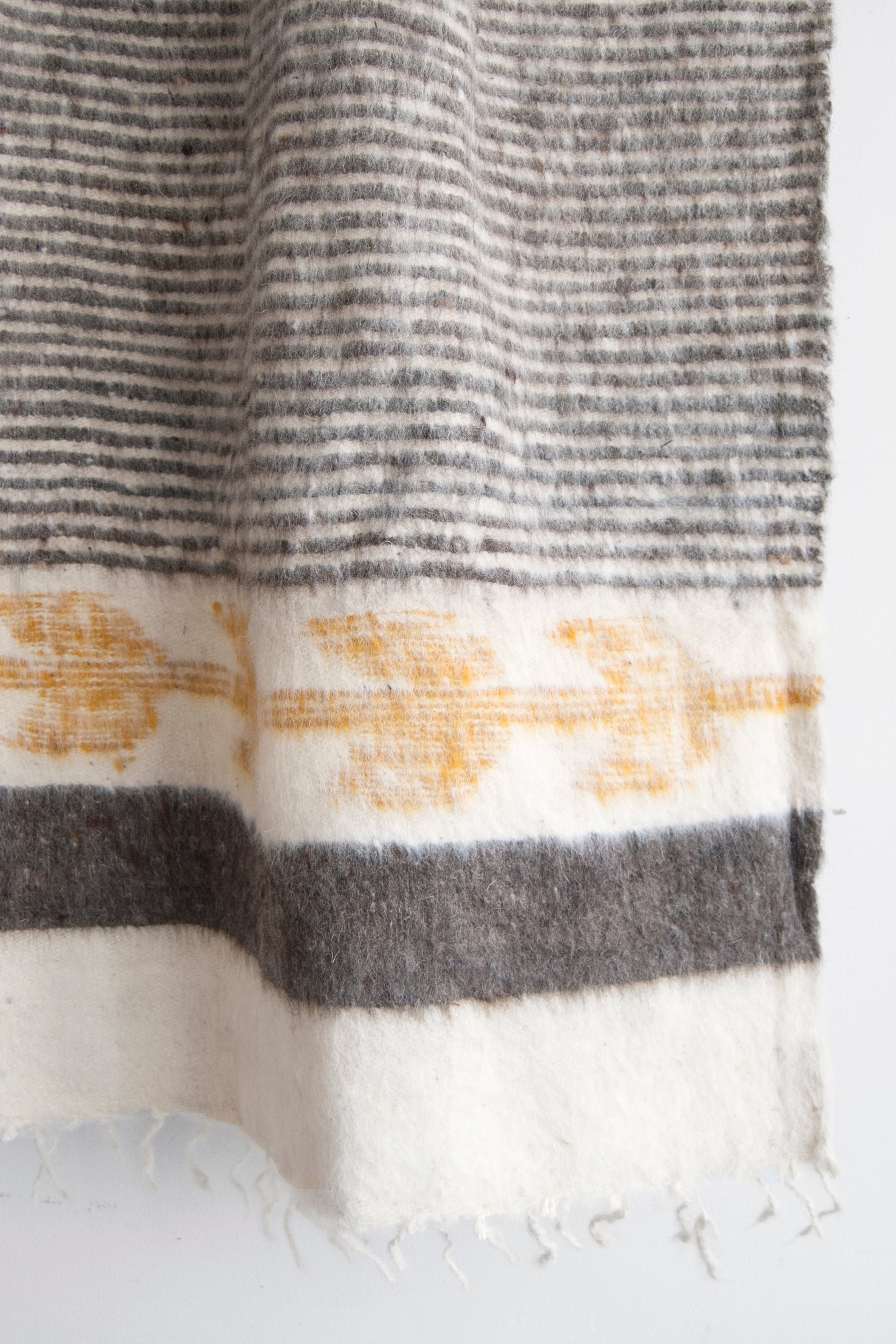 Detail of thin grey stripes and gold arrow motif on queen size ecru wool blanket