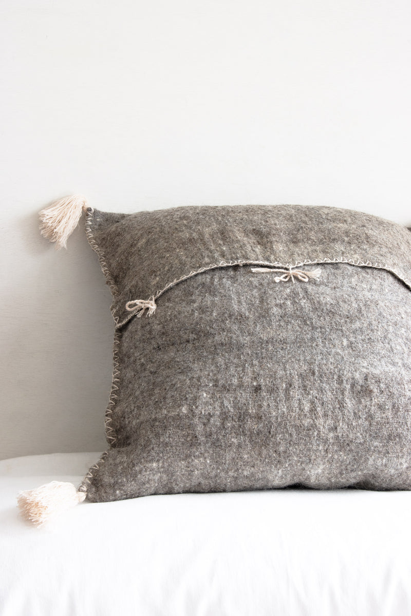 Reverse of grey square woven wool accent pillow showing back tie closures and cream tassels at each corner