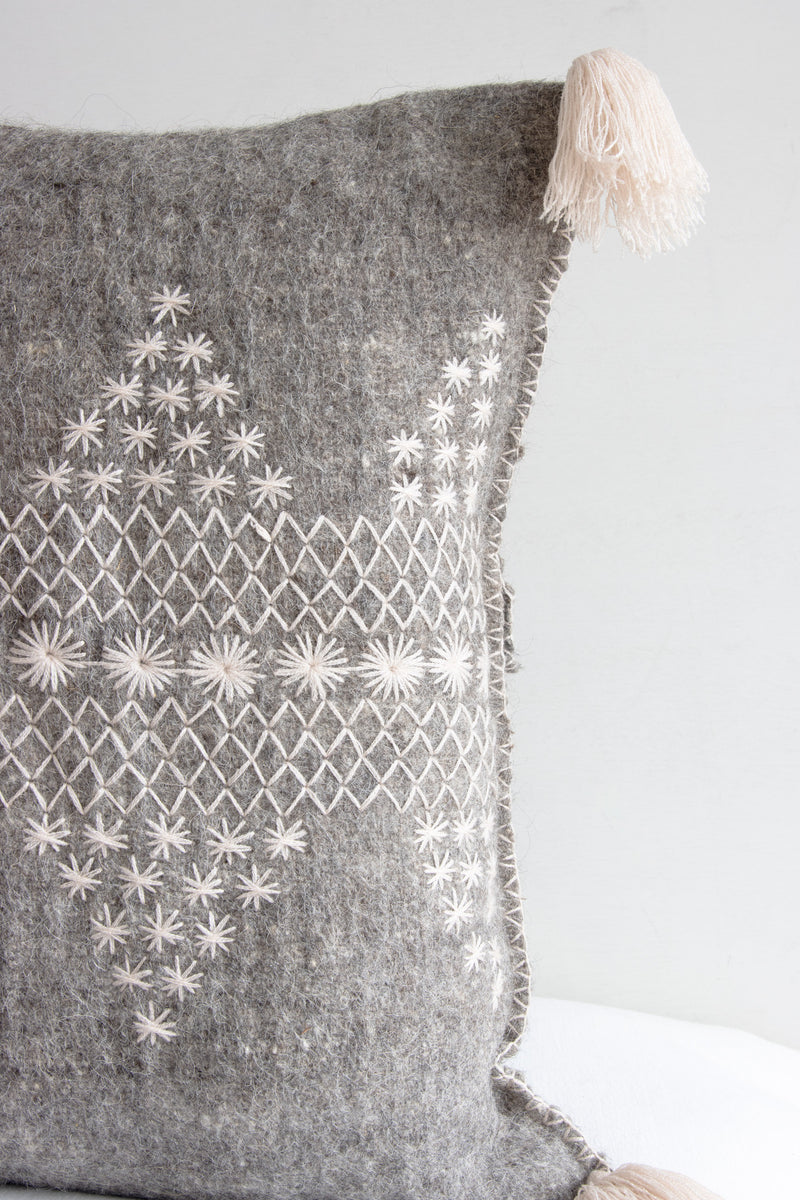 Detail of grey square woven wool throw pillow showing decorative cream embroidery and cream tassel