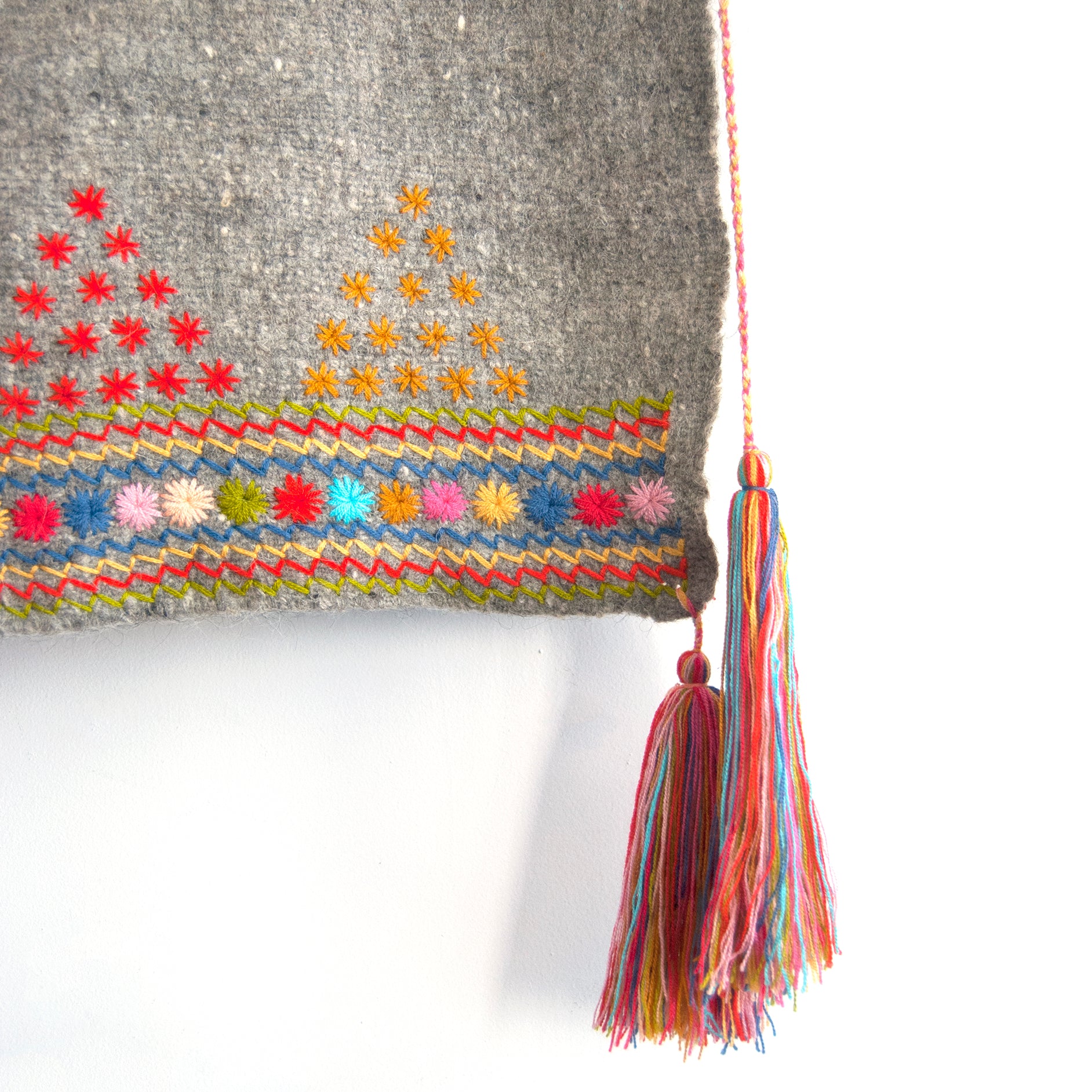 Detail of grey wool throw with colorful embroidered trim and multicolor corner tassels