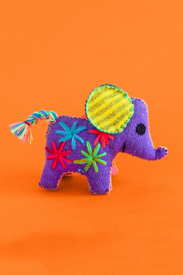 Colorful felt elephant plush toy with a multicolor braided tail and hand-embroidered features and star designs.