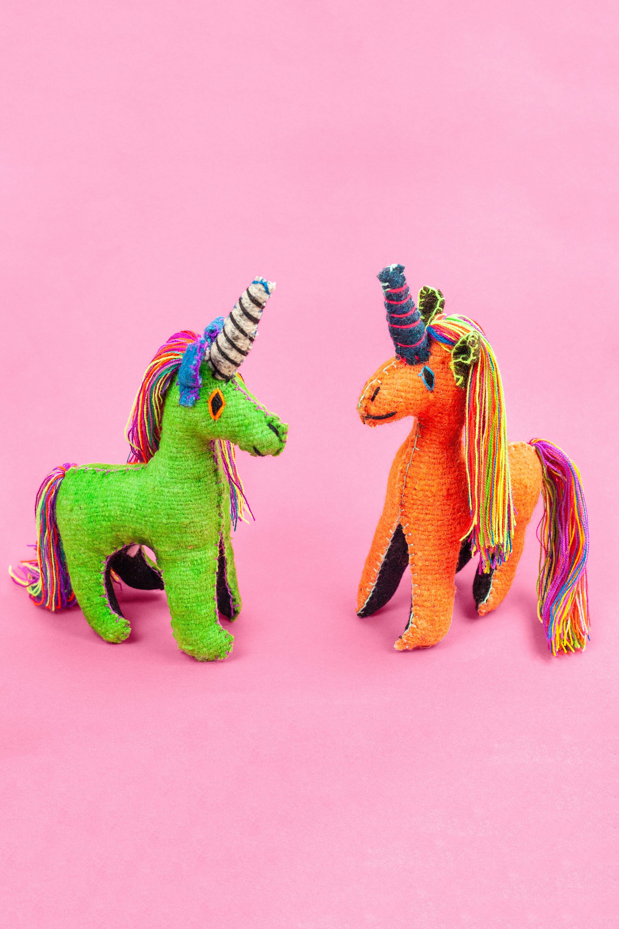 Two colorful felt unicorn plush toys with colorful fringe manes and tails and hand-embroidered features.