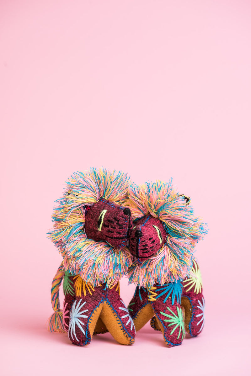 Two colorful felt lion plush toys with multicolor braided tails and fringe manes. Hand-embroidered features and star designs across the body.