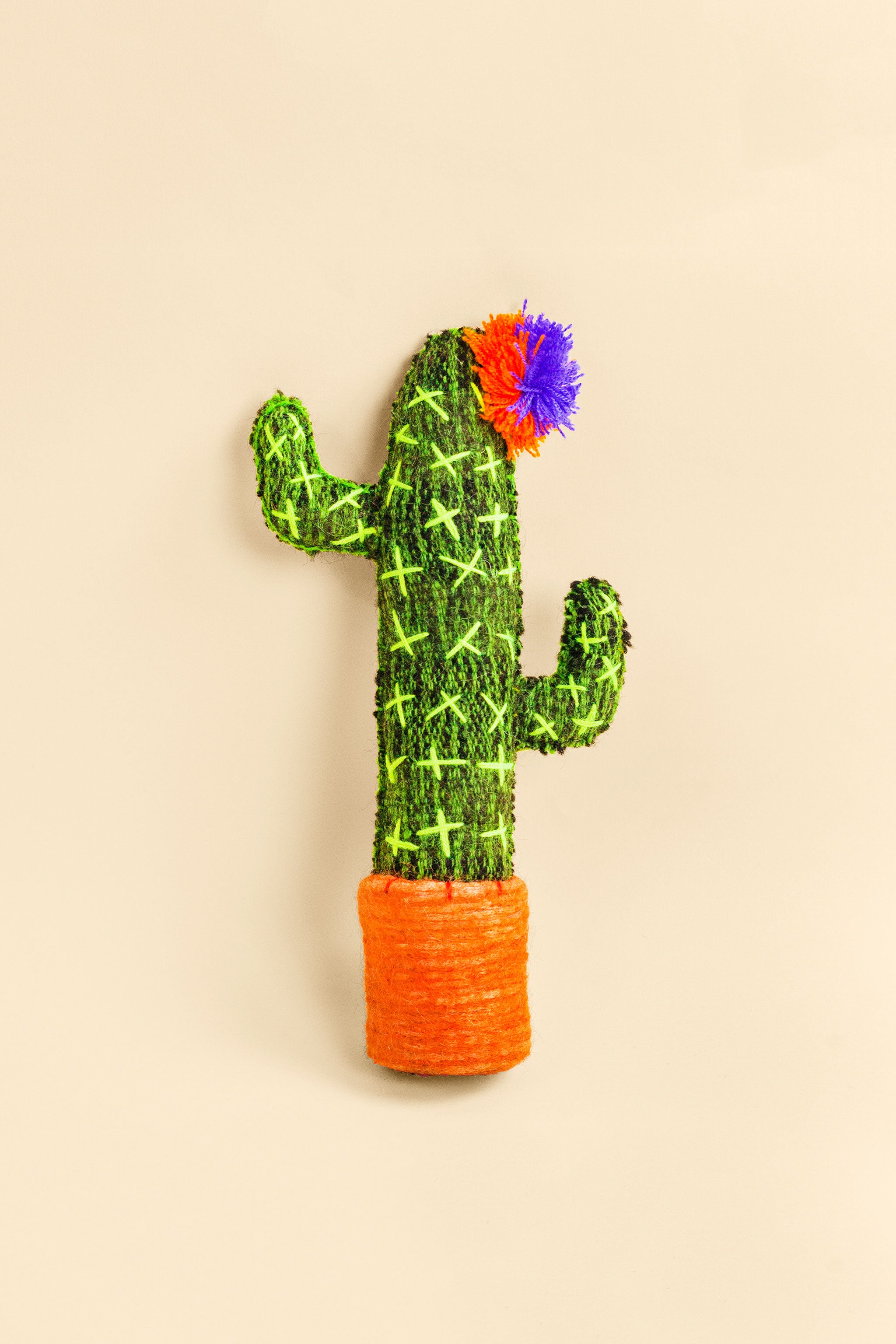 Standing green felt cactus plush toy with hand-embroidered thorns and a colorful pom pom flower on top.