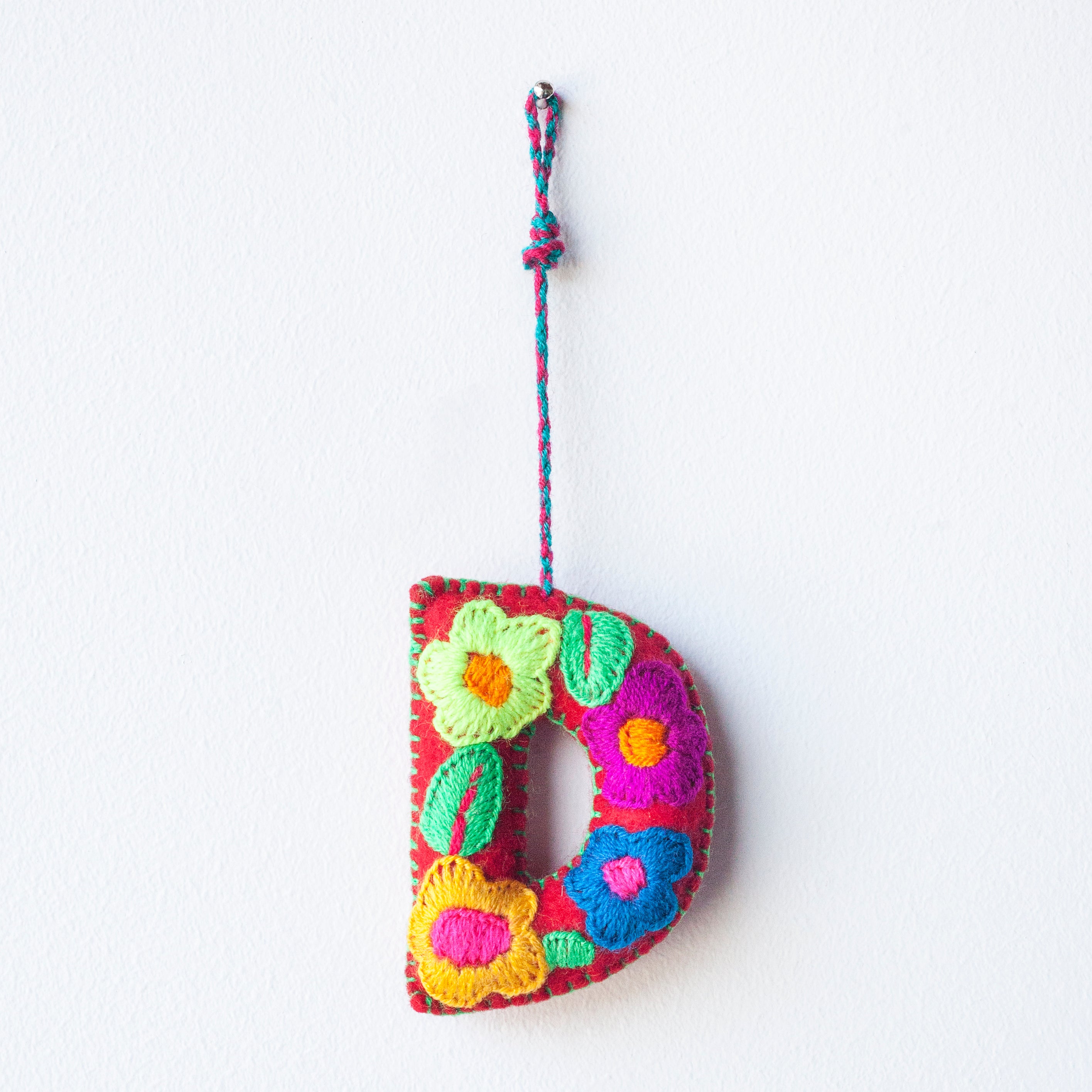 Colorful felt letter "D" with multicolor floral hand-embroidery hanging by a colorful string.