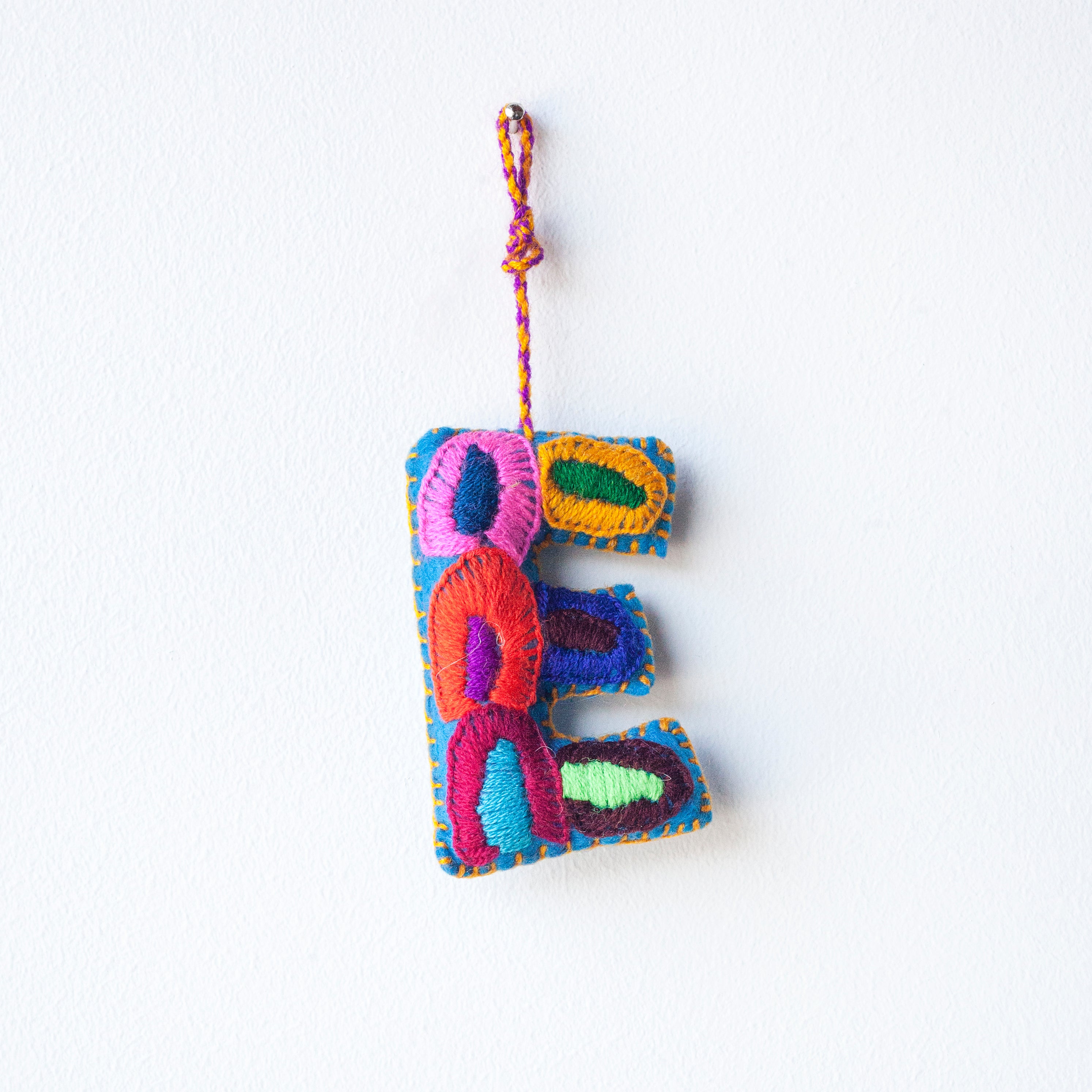 Colorful felt letter "E" with multicolor floral hand-embroidery hanging by a colorful string.