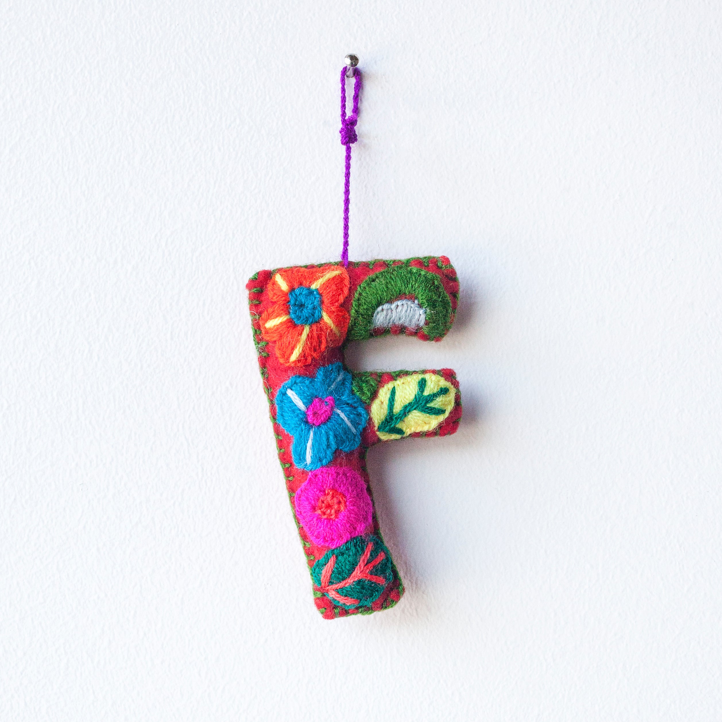 Colorful felt letter "F" with multicolor floral hand-embroidery hanging by a colorful string.