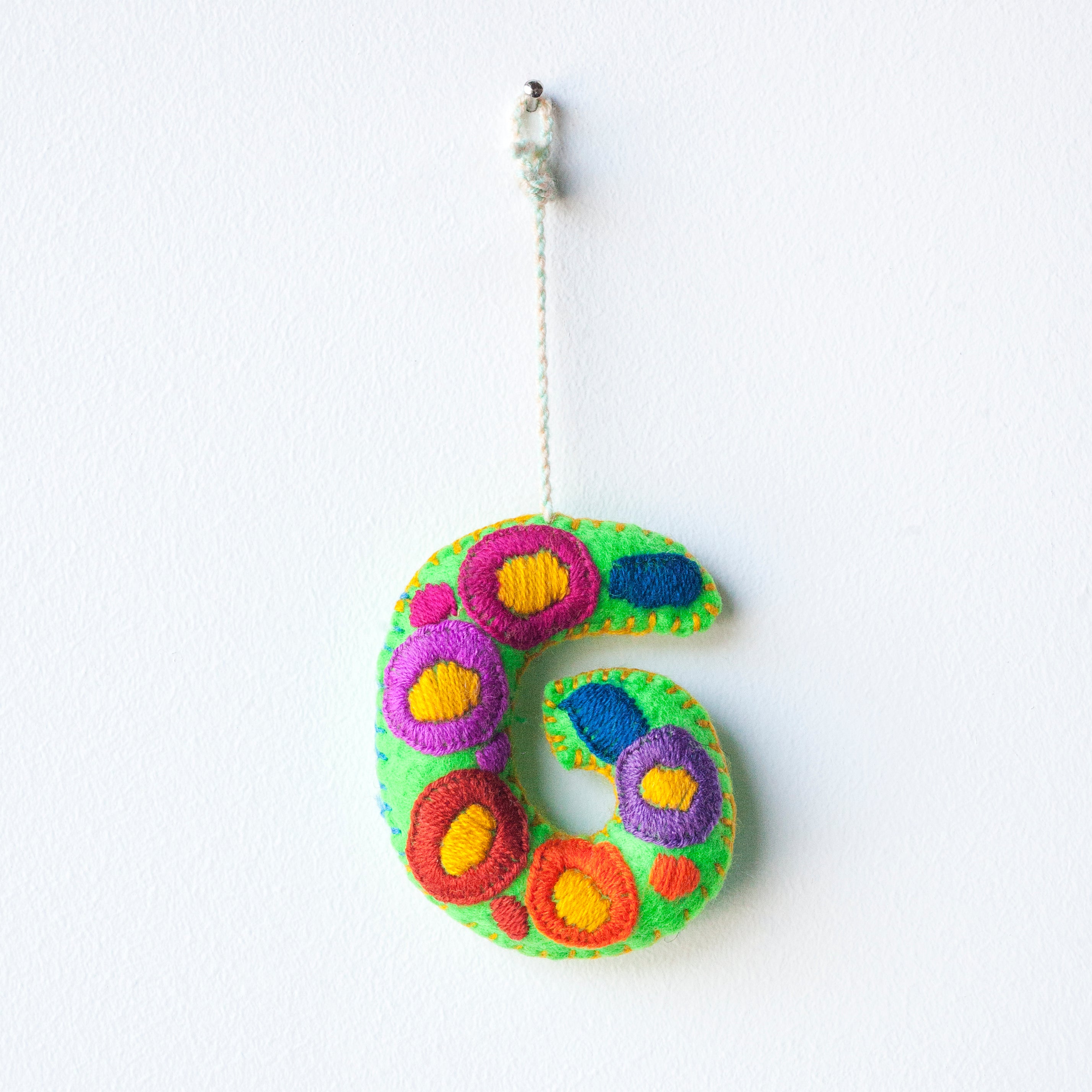 Colorful felt letter "G" with multicolor floral hand-embroidery hanging by a colorful string.