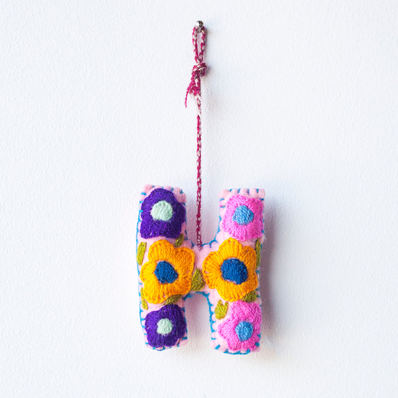 Colorful felt letter "H" with multicolor floral hand-embroidery hanging by a colorful string.
