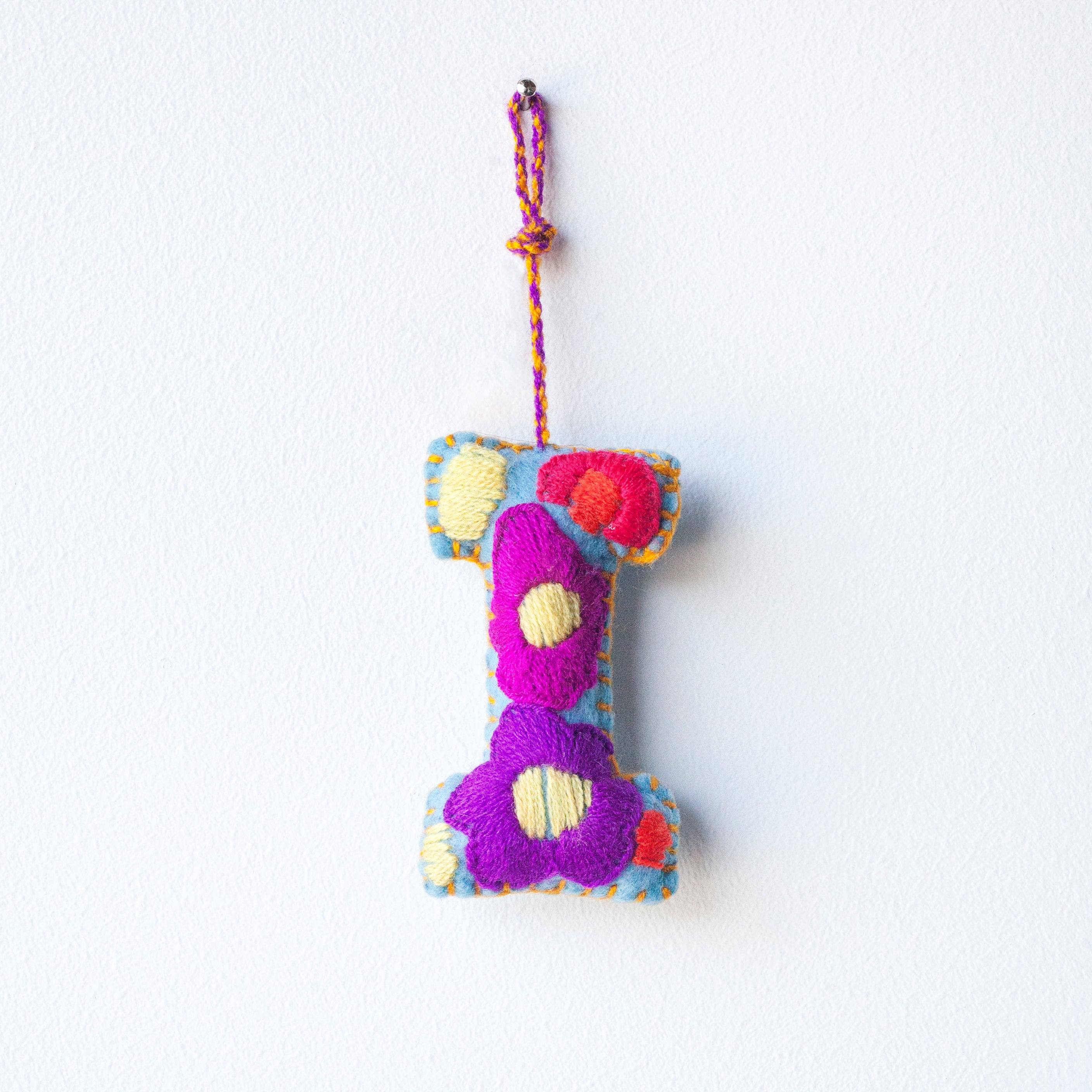 Colorful felt letter "I" with multicolor floral hand-embroidery hanging by a colorful string.