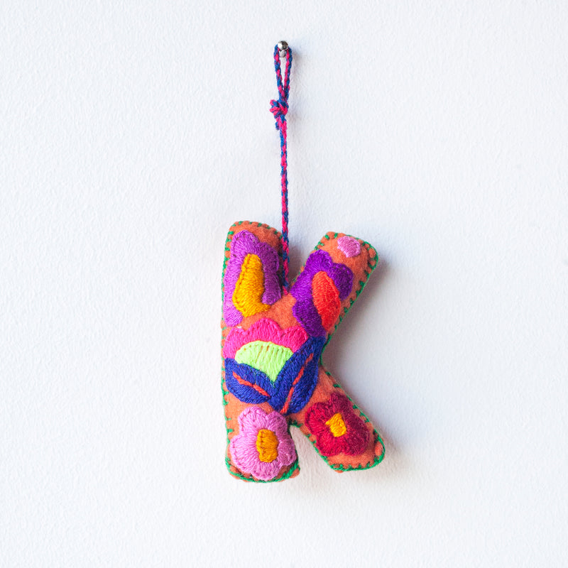 Colorful felt letter "K" with multicolor floral hand-embroidery hanging by a colorful string.
