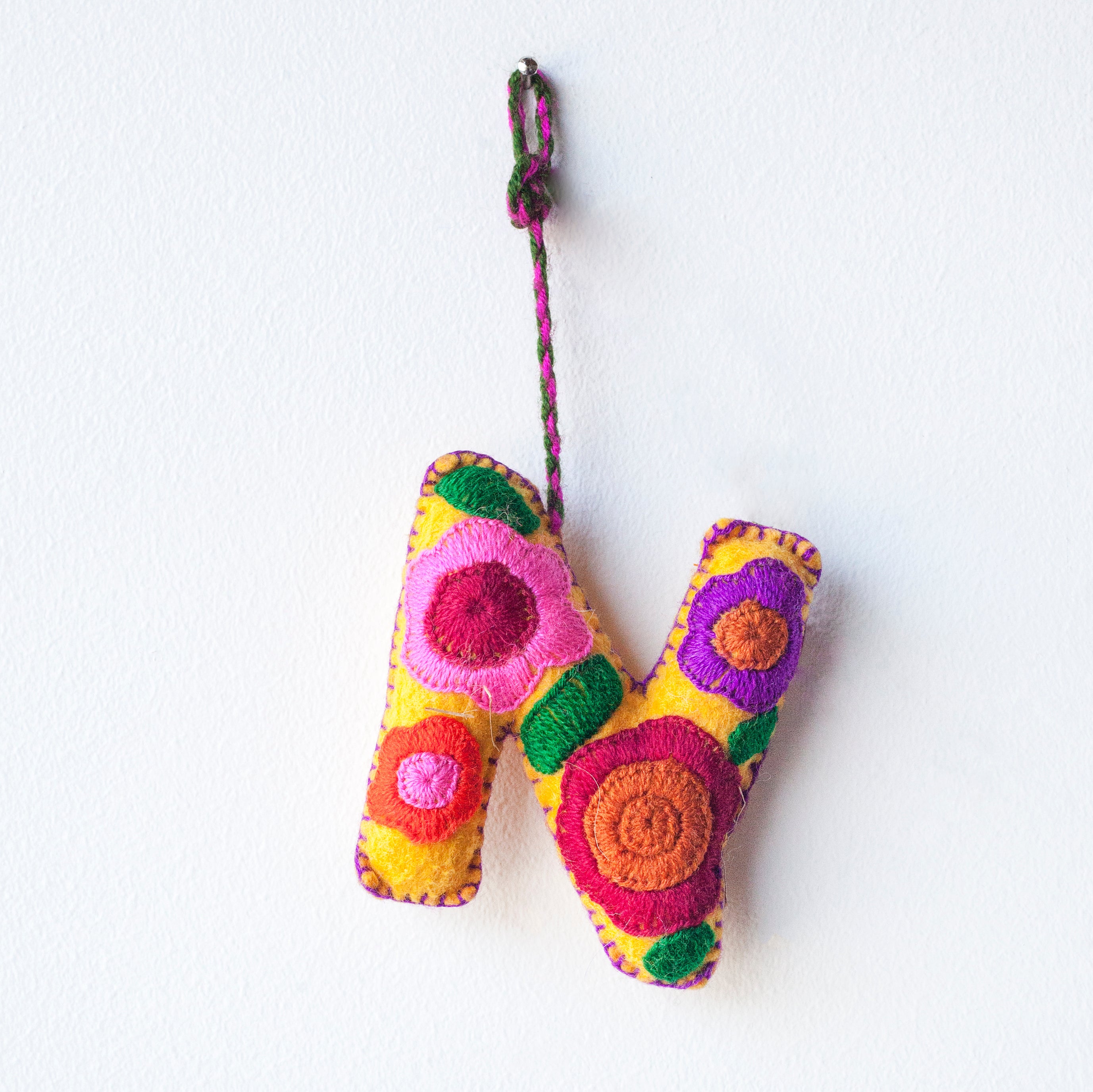 Colorful felt letter "N" with multicolor floral hand-embroidery hanging by a colorful string.