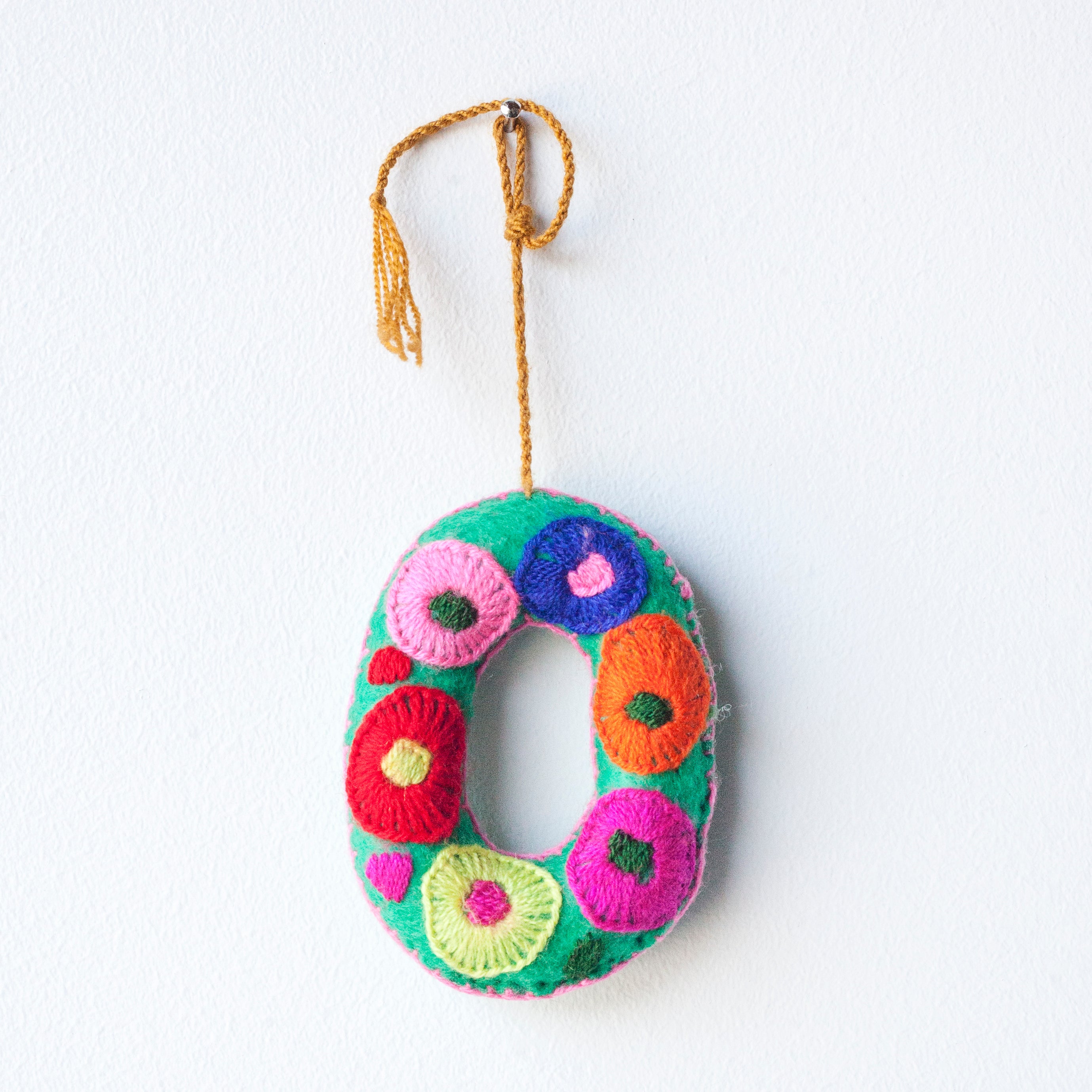 Colorful felt letter "O" with multicolor floral hand-embroidery hanging by a colorful string.