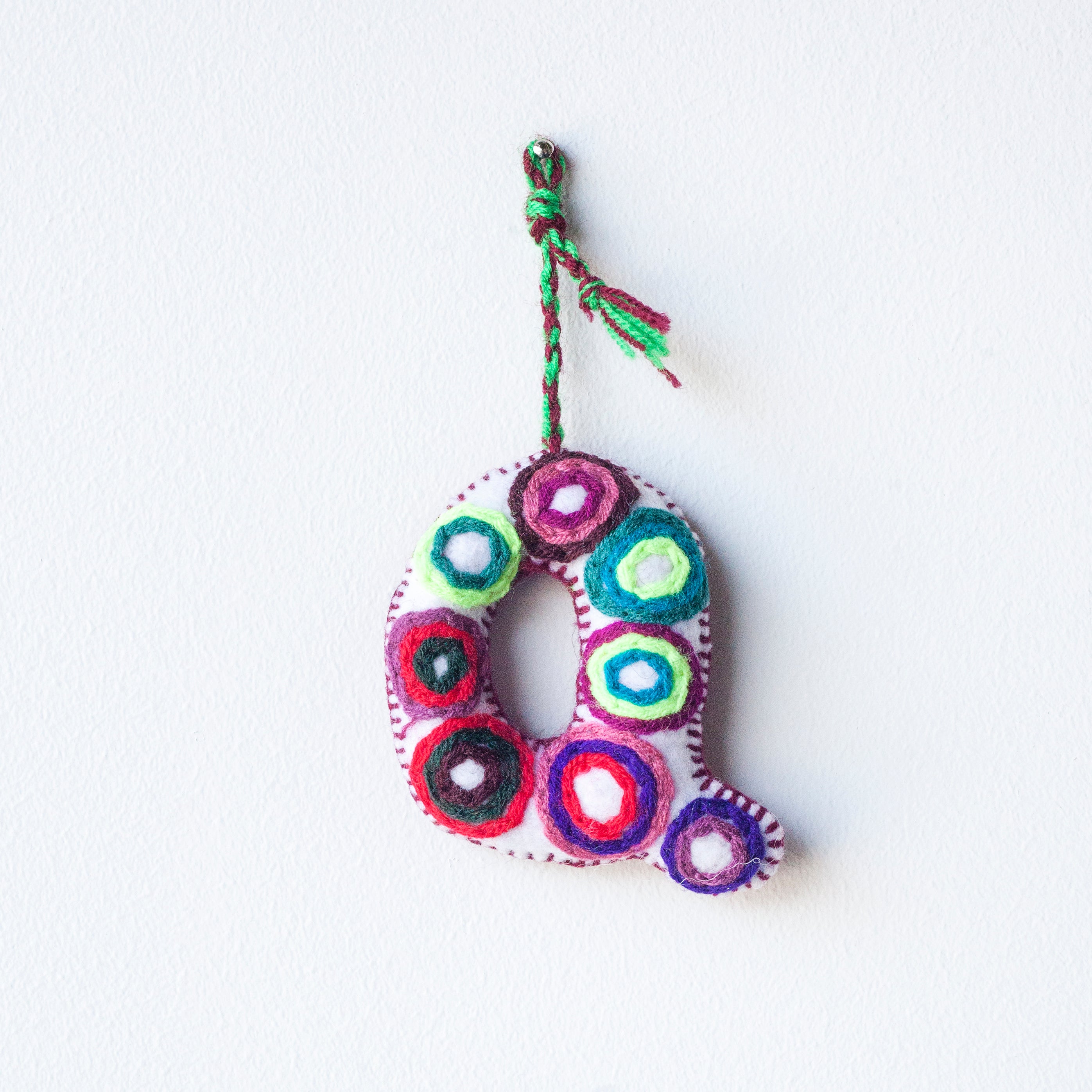 Colorful felt letter "Q" with multicolor floral hand-embroidery hanging by a colorful string.
