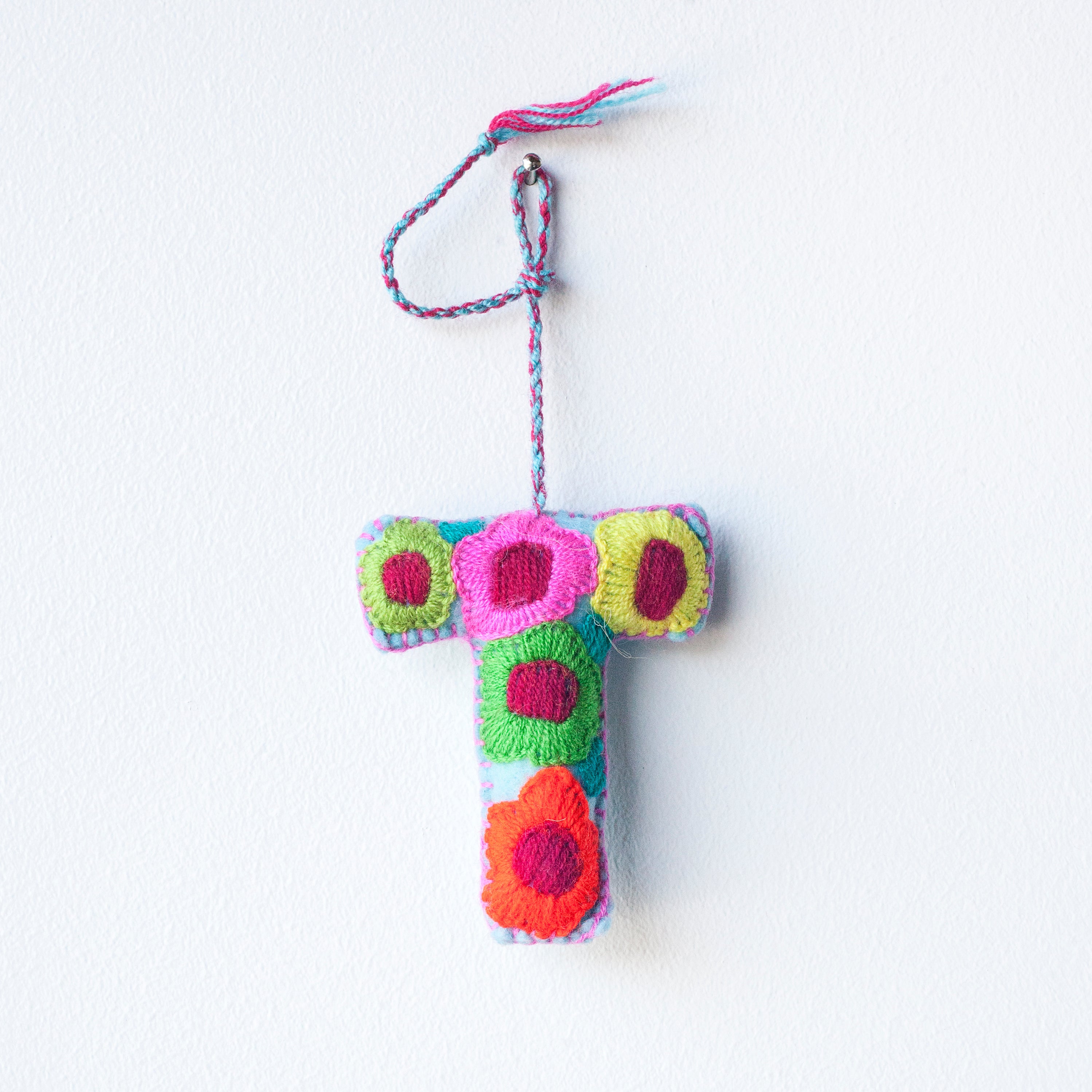 Colorful felt letter "T" with multicolor floral hand-embroidery hanging by a colorful string.