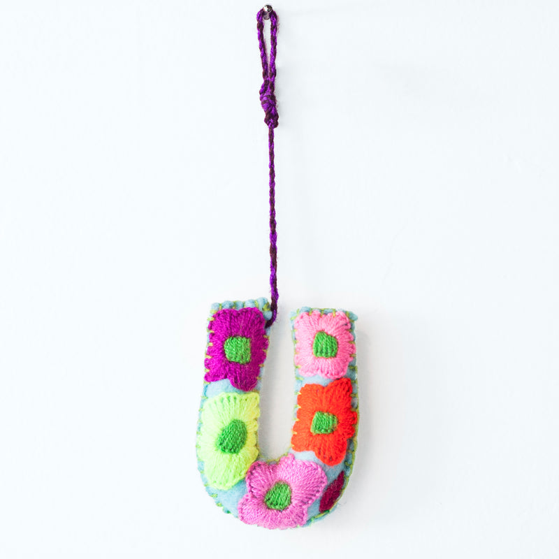 Colorful felt letter "U" with multicolor floral hand-embroidery hanging by a colorful string.