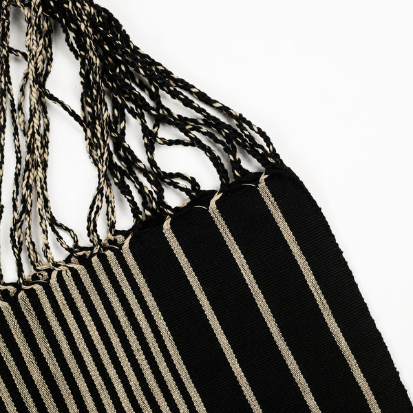 Detail of black tote bag showing the weave, vertical off-white stripes, and black/off-white braided straps.