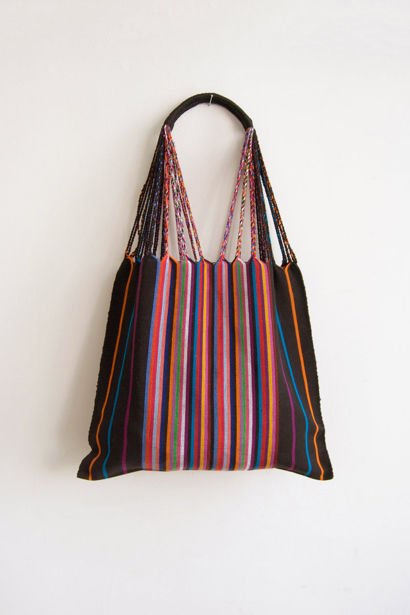 Woven black tote bag with vertical multicolor stripes and multicolor/black braided straps attached to a curved black handle.