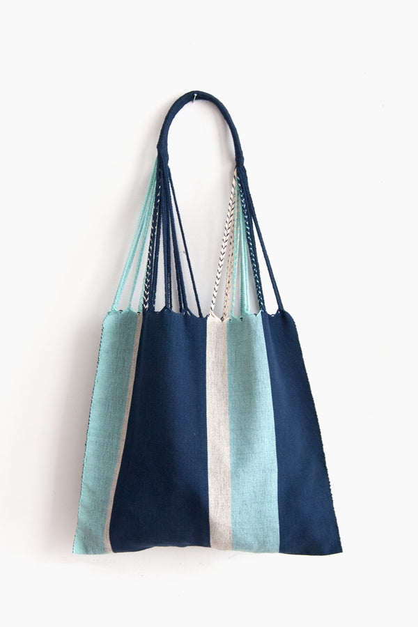 Woven tote bag with vertical navy, white, and light blue stripes and braided straps attached to a curved navy handle.