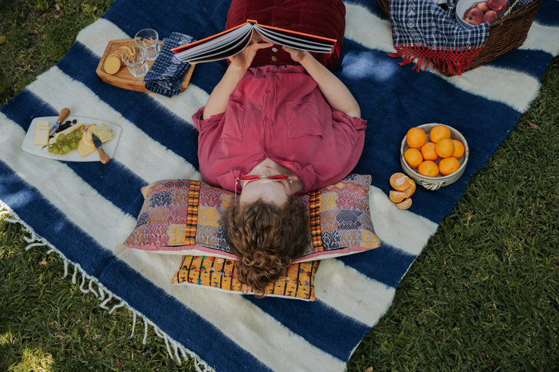 Woman reading at a picnic on top of a blue indigo and ecru wool blanket outside