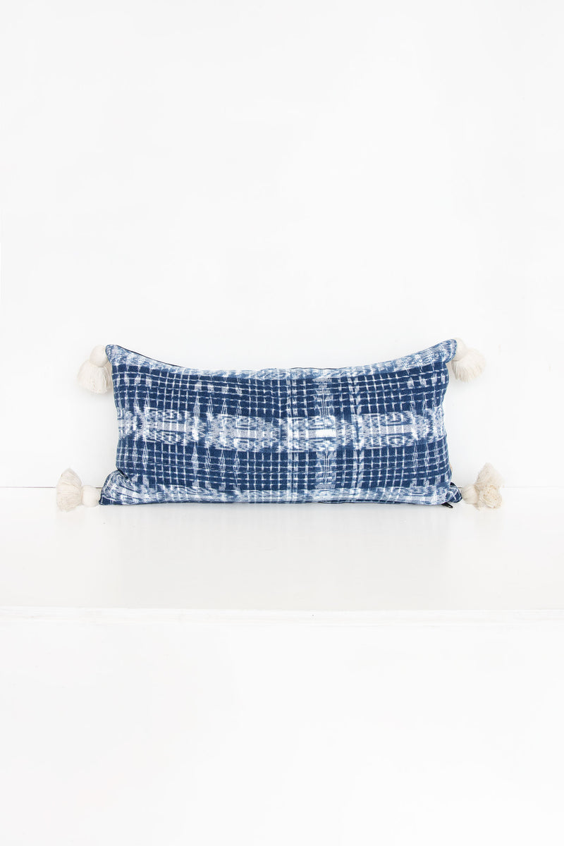 Blue and white pattern textile lumbar pillow with white tassels at each corner.