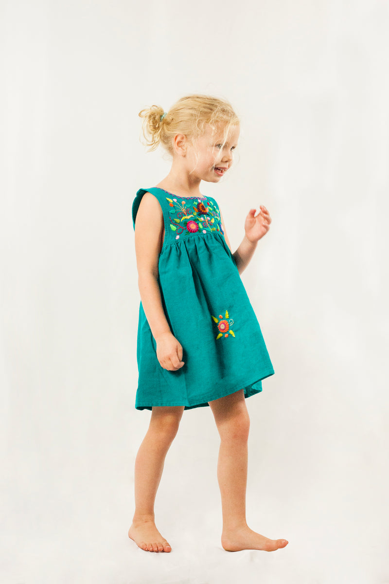 Child wearing a sleeveless teal knee-length sun dress. There are hand embroidered floral elements on the chest and skirt of the dress.