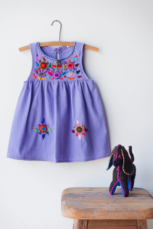 Kids sleeveless light purple sun dress hanging with multicolor hand-embroidered floral pattern on chest and two hand-embroidered flowers near the bottom of the skirt on the front left and right.