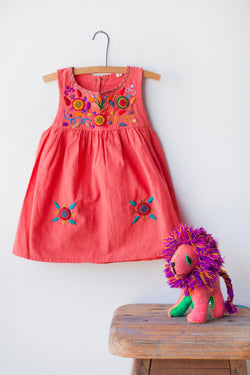 Kids sleeveless coral sun dress hanging with multicolor hand-embroidered floral pattern on chest and two hand-embroidered flowers near the bottom of the skirt on the front left and right.