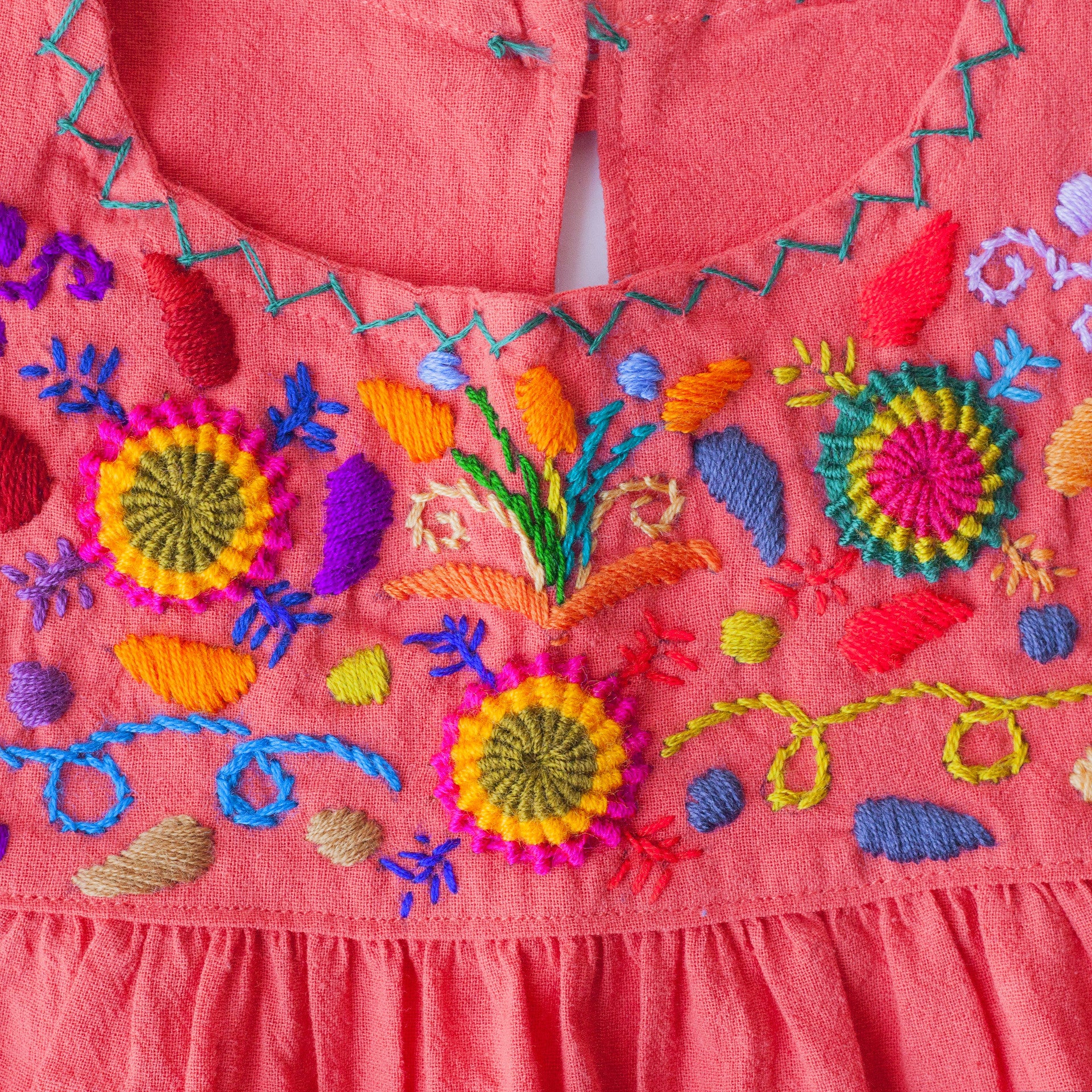 Detail of hand-embroidered multicolor floral pattern on chest and hand-done cross-stitch along neckline. 