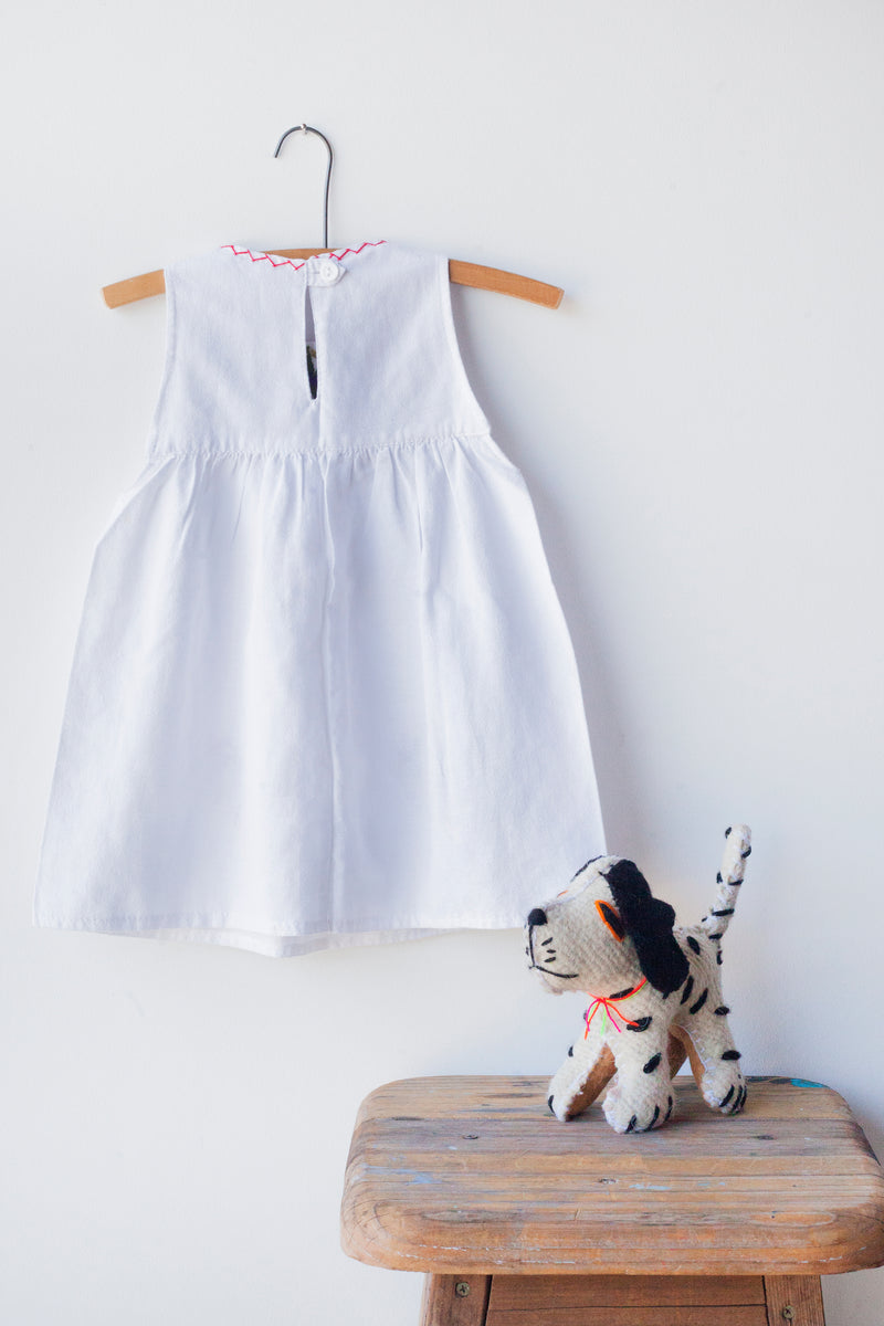 Reverse of kids sleeveless white sun dress, showing white button closure at neck.