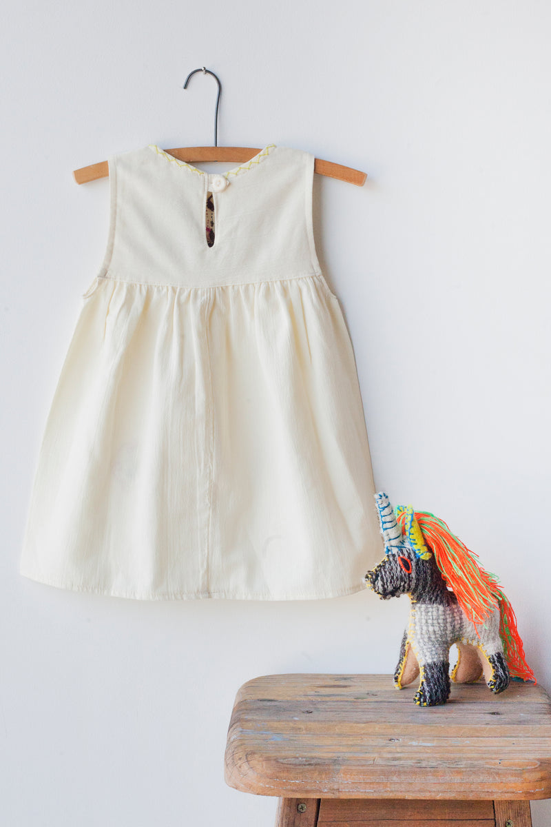 Reverse of kids sleeveless cream sun dress, showing cream button closure at neck.