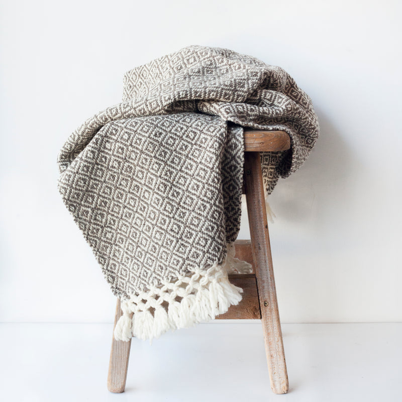 Brown and white wool throw blanket woven in a diamond pattern with tied tassels at each end draped over a wood stool