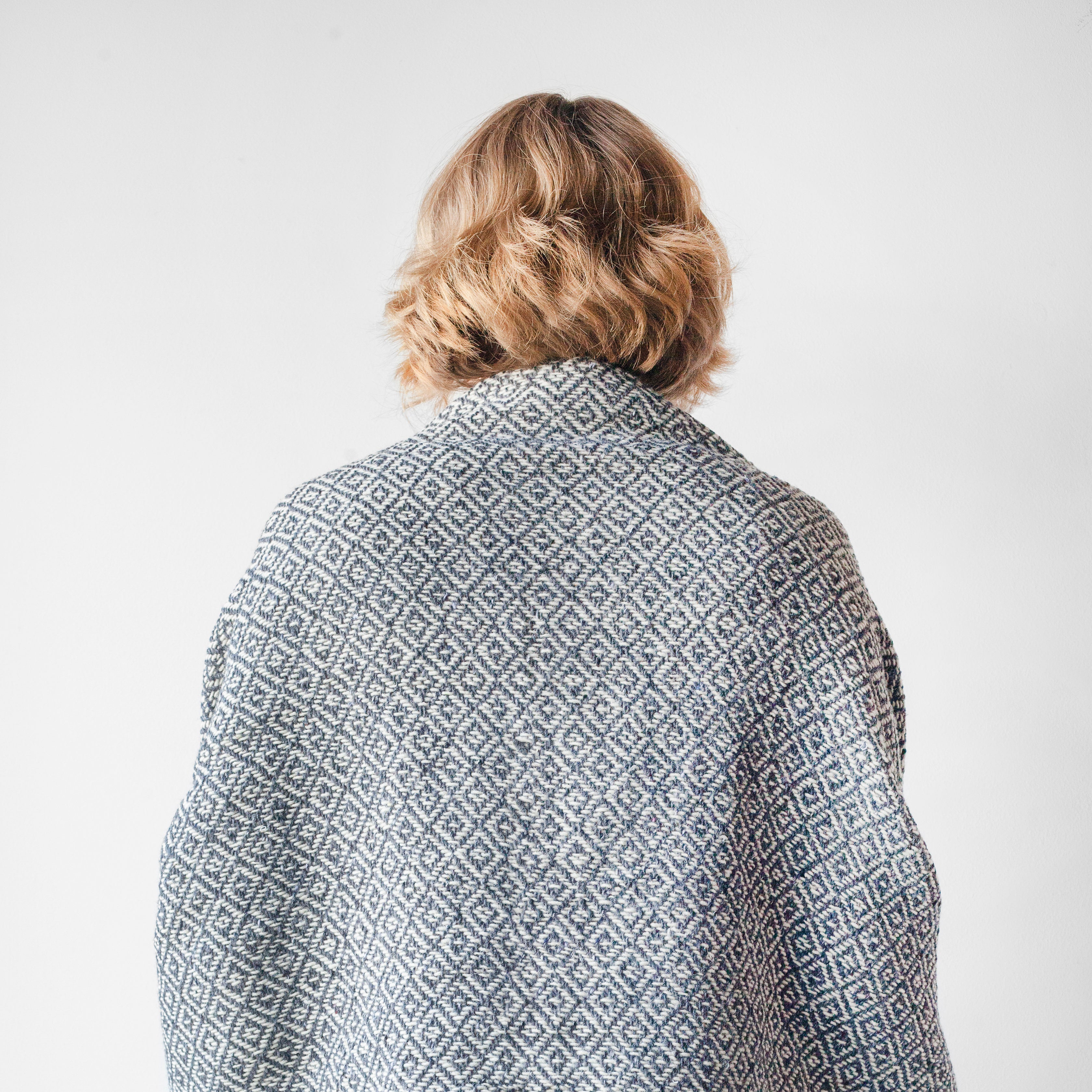 Charcoal grey and white wool throw blanket woven in diamond pattern being worn over the shoulders as a shawl