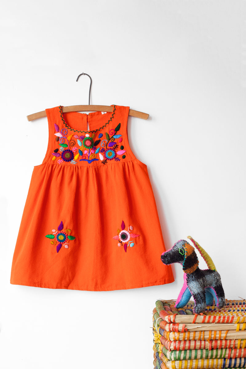 Kids sleeveless orange sun dress hanging with multicolor hand-embroidered floral pattern on chest and two hand-embroidered flowers near the bottom of the skirt on the front left and right.