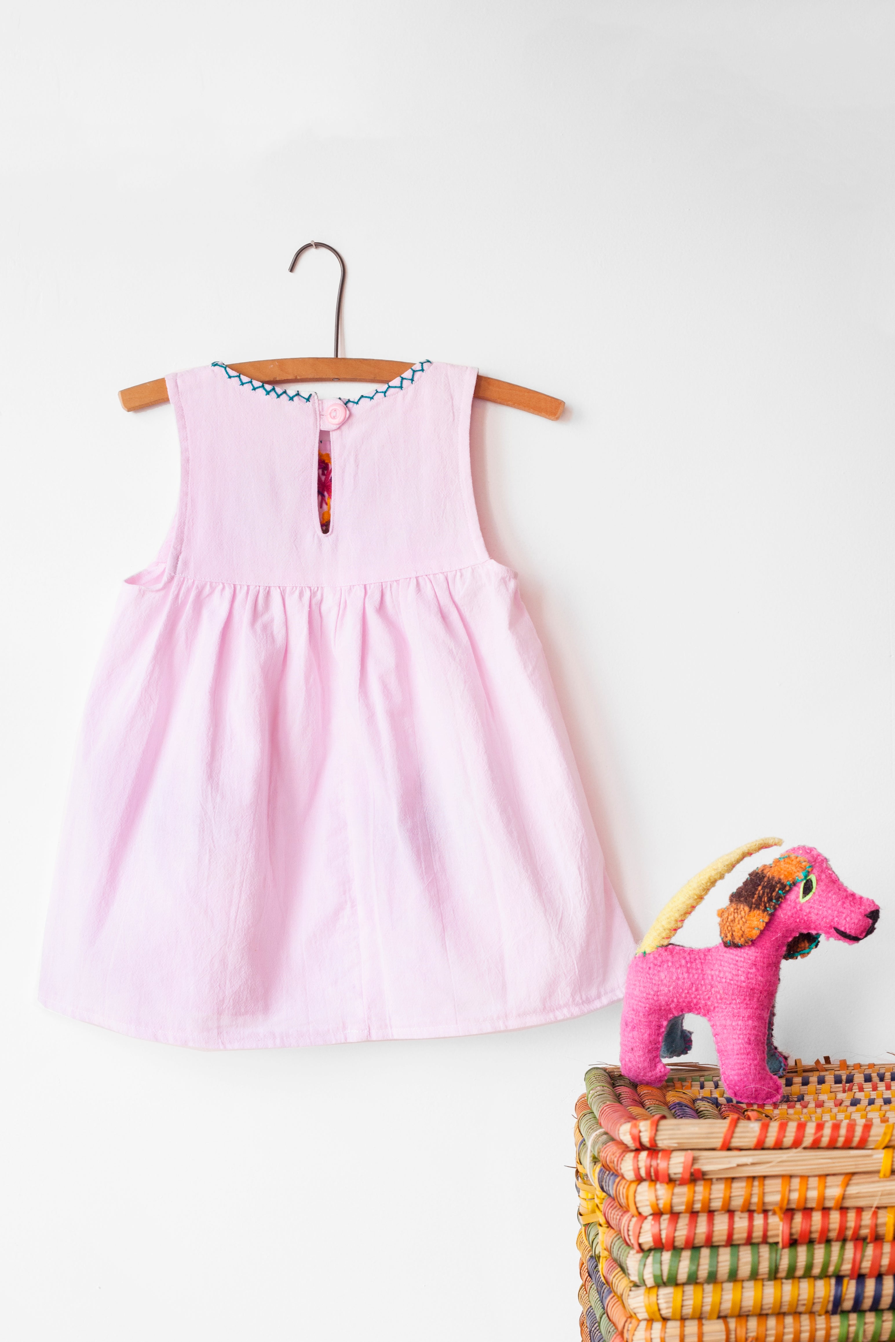 Reverse of kids sleeveless light pink sun dress, showing light pink button closure at neck.