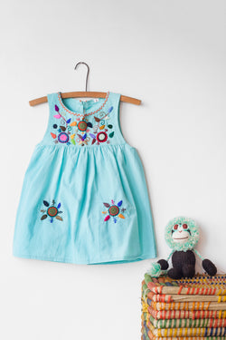 Kids sleeveless light blue sun dress hanging with multicolor hand-embroidered floral pattern on chest and two hand-embroidered flowers near the bottom of the skirt on the front left and right.